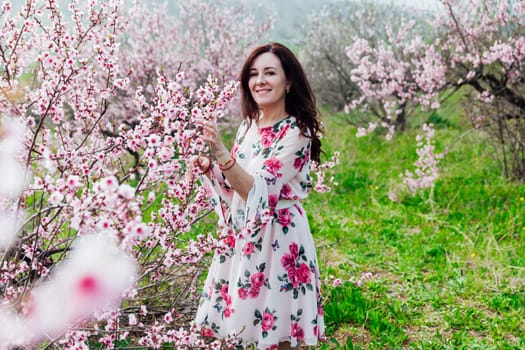 Brunette woman smiling in flower dress in spring blooming garden