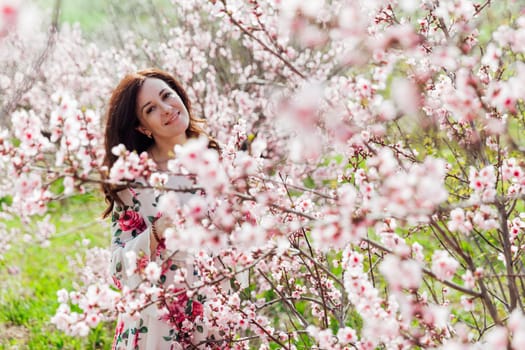 Brunette woman walking in flower dress in spring blooming garden