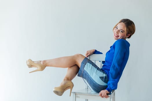 Portrait of a beautiful slender woman in a blue dress sitting on an armchair in a white room