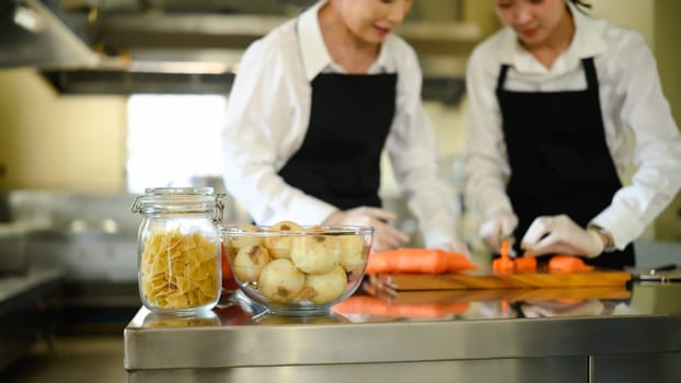 Fresh ingredients prepared for cooking with chefs chopping vegetables in the background..