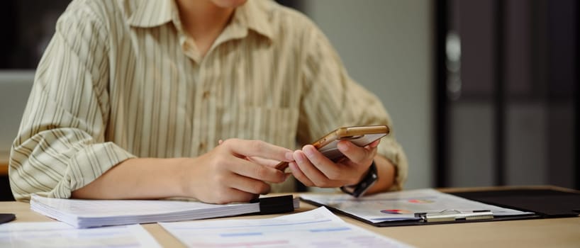 Close up of businessman using smartphone at office desk with financial documents.