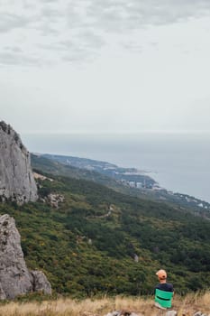 Boy hiking looking landscape at sky with clouds and green forest from mountain top