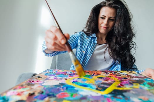 Brunette artist painting a picture on an easel with a brush with paints