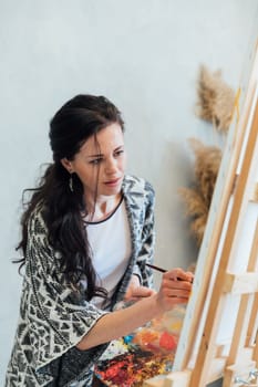 Brunette artist painting a picture on an easel with a brush with paints