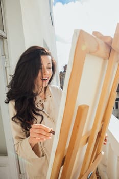 brunette artist paints a picture with a brush with paints and smiles
