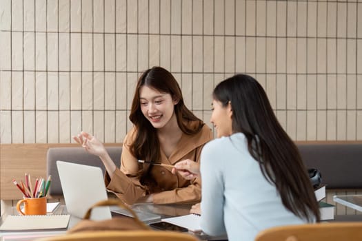 In a bright study environment, two friends brainstorm together, using their laptop and notes to foster deep academic conversation.