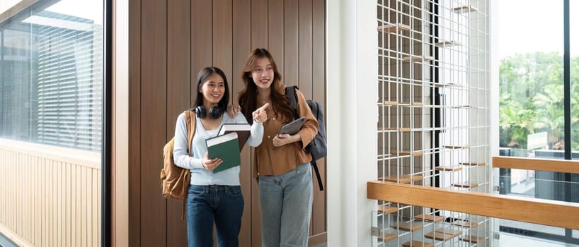 Two university friends pose together in a bright corridor, excited about their upcoming classes and academic journey.