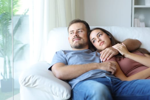 Happy couple sitting on a sofa looking outside through a window at home