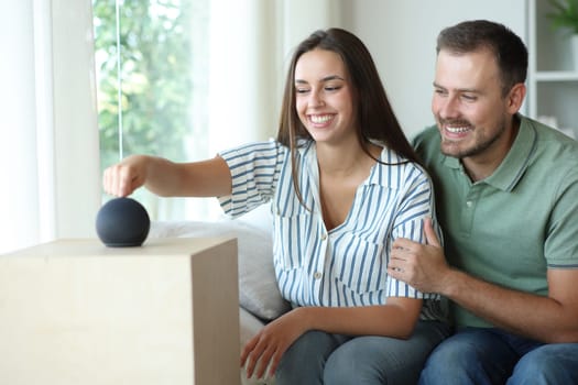 Happy couple starting new smart speaker sitting on a couch at home