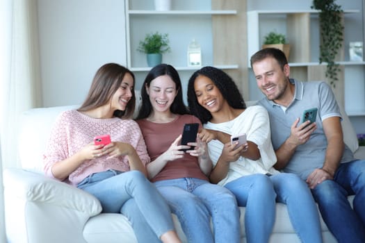 Happy inrterracial group of friends checking phones sitting on a couch at home