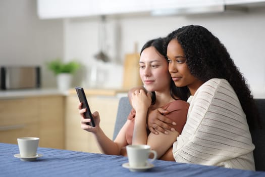 Interracial lesbian couple using phone in the kitchen at home