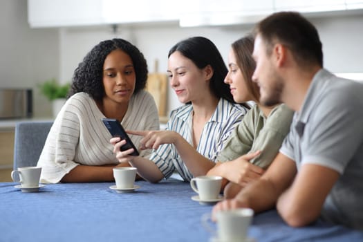 Interracial friends using smart phone in the kitchen at home
