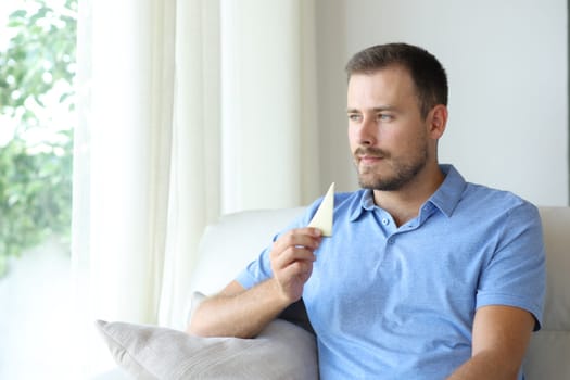 Man eating cheese looking away sitting on a couch at home
