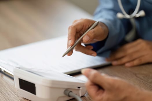 In a clinical setting, a nurse points to a health monitor and explains the medical data to a patient, ensuring they understand the importance of their results.