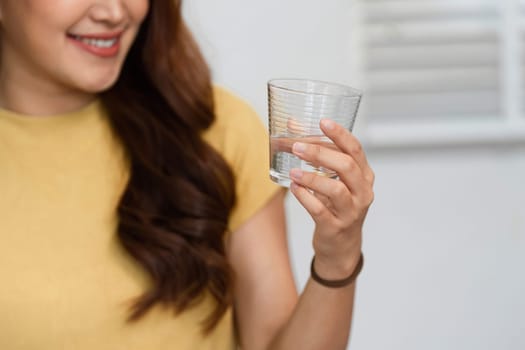 A woman beams with joy as she holds a glass of water, symbolizing positivity and hydration on a bright morning, ready to embrace the day ahead.