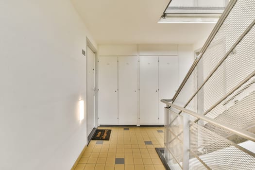 A sleek indoor corridor featuring contemporary design elements including a staircase and storage lockers along the walls, illuminated by natural light.