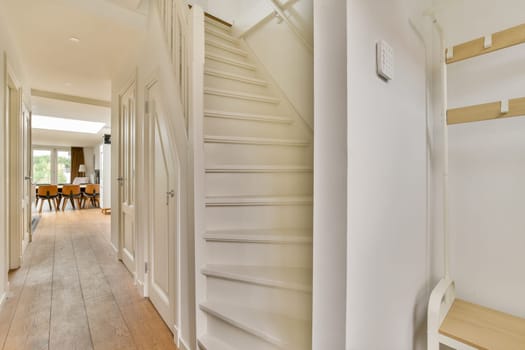 A spacious interior view showcasing a modern hallway leading to a staircase, illuminated by natural light, complementing contemporary design elements.