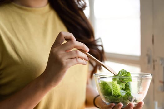 A woman prepares to savor her healthy salad, poised to enjoy a mindful eating moment in her bright and cheerful kitchen setting.