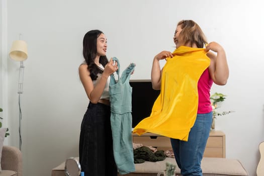 These two friends excitedly showcase vibrant dresses in their trendy living room, capturing the fun of their fashion adventure and companionship.