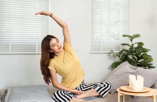 A young woman performs gentle stretching on her couch, promoting health and well-being as part of her morning routine.