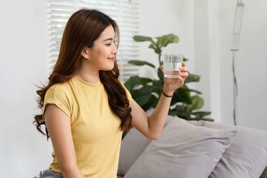 A woman sits comfortably on her couch, savoring a glass of water as she welcomes the new day, focusing on well-being and hydration.