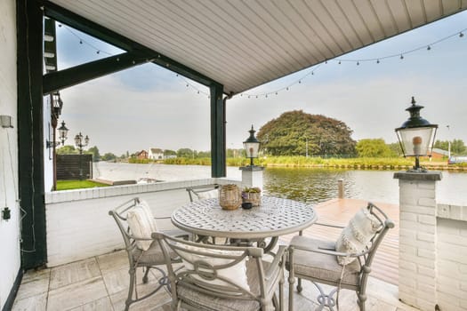 A charming outdoor patio featuring a round table and chairs, surrounded by greenery and looking out over calm waters, creating a perfect relaxation spot.