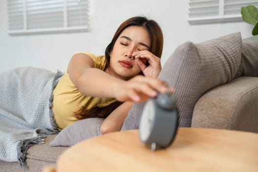 A young woman is waking up from her sleep, reaching out to turn off her alarm clock, ready to start her morning routine with energy.