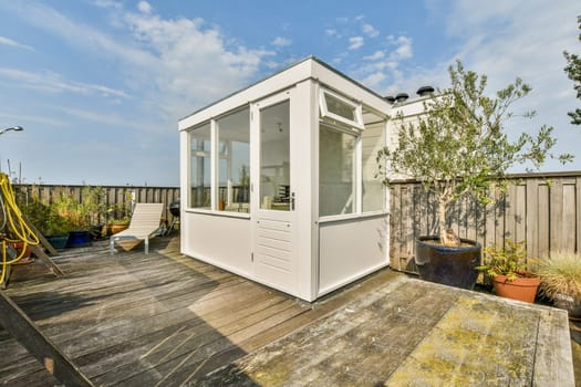 A beautifully designed modern outdoor living space featuring a glass enclosure, wooden deck, and potted plants, ideal for relaxation and enjoyment.