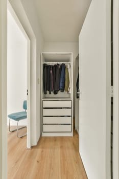 A tidy and modern interior featuring a wardrobe with clothes and a simple chair. The design emphasizes minimalism and functionality.