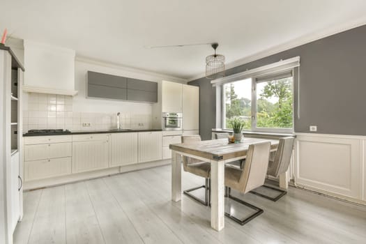 A stylish modern kitchen featuring sleek cabinetry, a dining table, and ample natural light from a large window, creating an inviting atmosphere.
