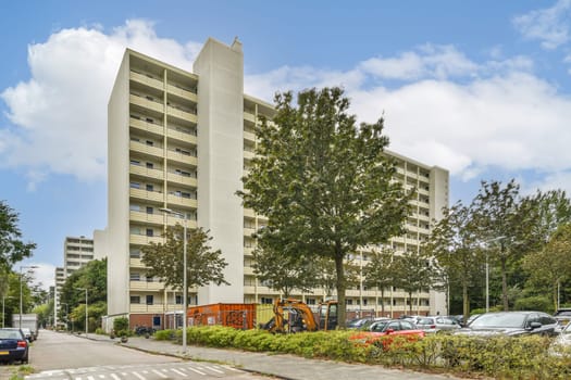 A contemporary multi-story residential building is captured, surrounded by lush green trees and clear sky, showcasing urban living harmoniously blended with nature.