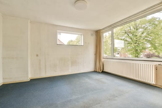 A spacious, empty room featuring a large window that offers a glimpse of greenery outside. The walls are bare, presenting a minimalist aesthetic.