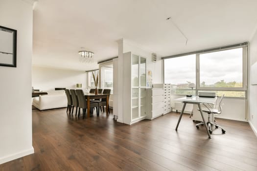 Spacious modern interior featuring a dining area and a workspace. Large windows provide ample natural light, enhancing the open atmosphere.