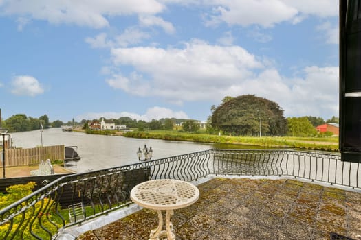 A picturesque view from a balcony overlooking a serene river, surrounded by lush greenery and quaint houses under a cloudy sky.
