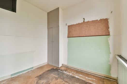 An empty room showing a mix of white and green walls, with one side partially covered and showing bare patches. The floor has been stripped down, presenting a raw feel.