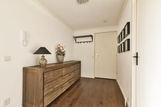 A stylish, modern hallway featuring a wooden storage unit, lamp, and decorative items, creating an inviting atmosphere.