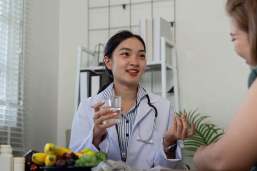 A nutritionist engages a patient in conversation about healthy dietary choices, emphasizing the importance of hydration with a glass of water and discussing various fruits and vegetables.