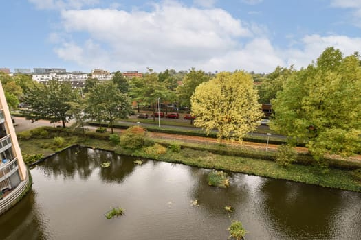 A picturesque landscape showcasing a peaceful park with lush trees lining a calm body of water, reflecting the blue sky and clouds above.