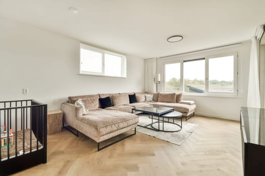 A modern living room showcasing a stylish sofa, coffee table, and large windows for natural light. The decor is minimal, creating a cozy atmosphere.