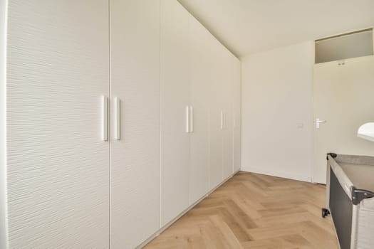 A sleek, white wardrobe complements the minimalist design of a spacious interior, featuring clean lines and natural wood flooring for a contemporary look.