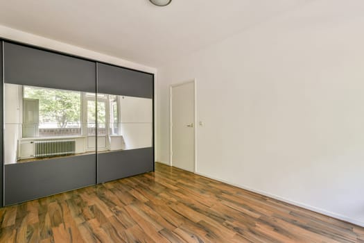 A minimalistic interior space featuring a stylish mirror wardrobe and wooden flooring, creating a serene and spacious ambiance.