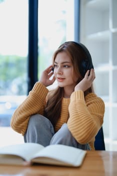 Young woman enjoying a relaxing music break at her desk while using headphones, writing in a notebook, and working on her laptop for calm inspiration.