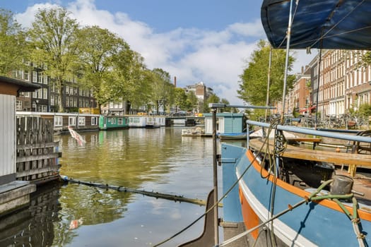 Picturesque view of a canal in Amsterdam featuring houseboats alongside lush trees and charming architecture under a bright sky.