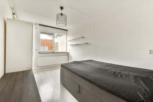 A stylish minimalist bedroom featuring a single bed, modern light fixture, and large window, creating a serene atmosphere for relaxation.