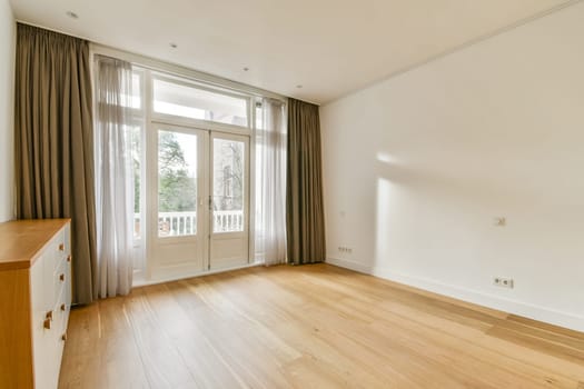 A bright, airy room featuring large windows that invite natural light, minimalist furnishings, and a warm wooden floor, creating a serene atmosphere.