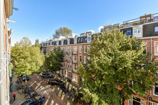 A picturesque view of a tree-lined Amsterdam street featuring traditional architecture and parked bicycles under a clear blue sky.