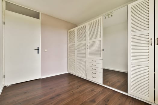 A modern minimalist interior featuring a sleek mirrored wardrobe and wooden flooring, creating an open and spacious atmosphere ideal for contemporary living.