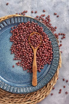 Ceramic blue plate full of dried red azuki beans with a wooden spoon on grey table top view, copy space. Healthy vegetarian food, legumes protein source. Traditional East Asian cousin ingredient
