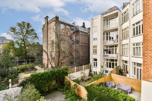 A contemporary apartment building facade juxtaposed with a lush garden and a brick structure, showcasing urban life and nature's harmony.