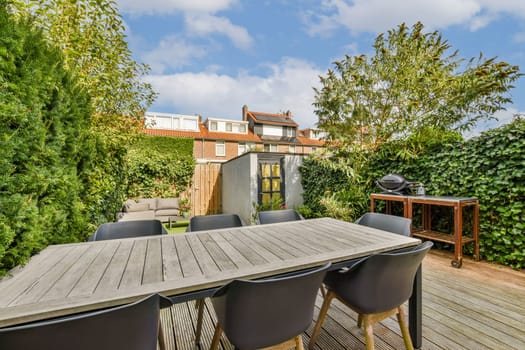 A stylish outdoor patio featuring a spacious wooden table surrounded by black chairs, set among lush greenery and blue skies. Ideal for gatherings and relaxation.